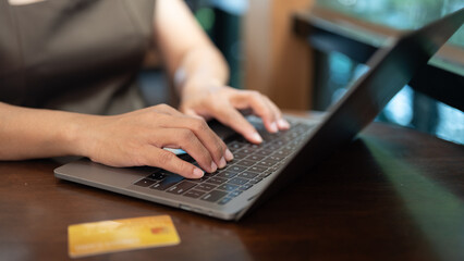 A woman is typing on a laptop with a credit card on the table. She is using the laptop to check her bank account