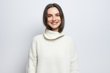Portrait of a beautiful young woman wearing a white sweater, on light gray background.