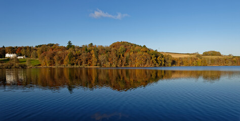 Clunie Loch near to Blairgowrie with the still waters capturing the reflections of the Trees and Forneth House under a clear blue Sky.