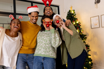 Young multiracial friends celebrating Christmas at home, wearing festive hats and laughing