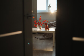 autumn still life with candles, flowers, twigs of red physalis in a vase in a cozy home interior