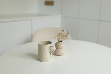 A cup of coffee and cream rustic white vase containing dried flowers on the table. Cozy living room decoration, beautiful home interior for design or print.
