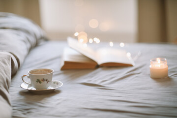 A cup of coffee and a book lying on the bed in a white bedroom