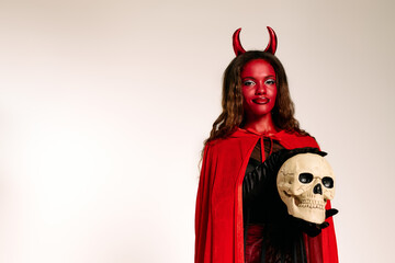A captivating woman in a devil costume highlights her look with a skull for Halloween.