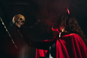 A striking woman dressed in a Halloween costume poses dramatically with a skull, creating intrigue.