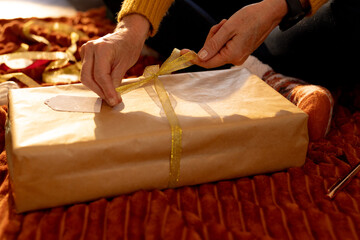 Wrapping Christmas gift with golden ribbon, hands tying bow on present, at home