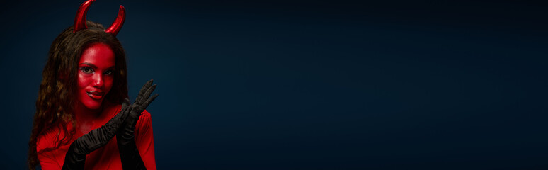 A stunning woman joyfully showcases her devil costume, radiating Halloween charm with flair.