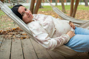 42 year old pregnant woman resting lying in a hammock in an autumn park. pregnancy after 40, 8...