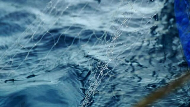 A closeup slow motion shot of a fishing net being pulled from the ocean on the side of a small fishing boat in Montego Bay, Jamaica