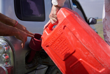 Fototapeta premium Close up view of two unrecognizable people loading gasoline into an suv from a red plastic container in a remote area.