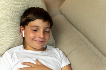 Portrait of happy boy listening to audiobook on headphones on sofa at home