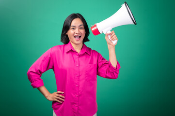 An Asian woman in a bright pink shirt against a green background, smiling while holding a megaphone...