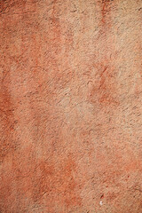 A close-up of a textured, red-orange wall showcasing rich, earthy tones and a rough, uneven surface. 