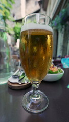 Chilled glass of beer on a restaurant table, condensation forming on the glass, fresh beer served outdoors with salad in the background