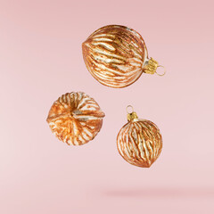 Christmas holliday image, Christmas bauble in shape of a golden walnuts falling in the air isolated on pink background