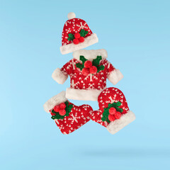 Christmas coat, hat and glove with mistletoe on blue background falling in the air
