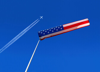 a passenger plane with vapour trails high in the blue sky and american windsock
