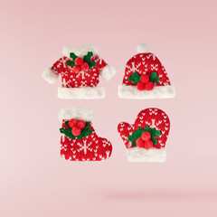 Christmas coat, hat and glove with mistletoe on pink background falling in the air