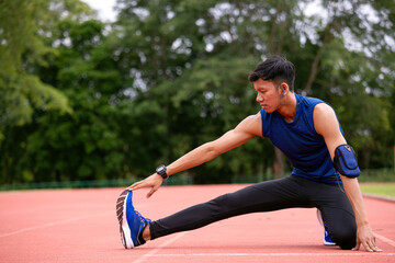 Young Athlete stretching on running track, reaching for foot to improve flexibility, wearing fitness gear and earphones with copy space