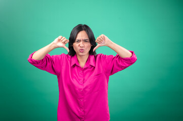 An Asian woman in a bright pink shirt poses against a green background, making a playful face and...
