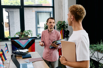 Two handsome men are having an animated conversation in a bright, modern office setting.