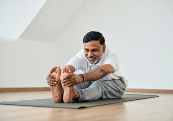 Indian senior man practicing yoga stretching on mat in minimalist room