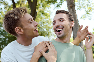 Two smiling men share a lighthearted moment surrounded by nature and sunlight.