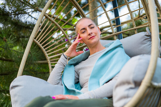 Young female cancer patient sitting on garden patio, rocking in a hanging chair. Health insurance, medical expenses, loss of income safety plan.
