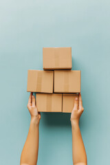 Hands holding cardboard shipping boxes on plain color background, copy space