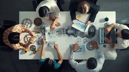 Top down aerial view of smart engineer team working together to design turbine engine. Professional technician discussing about jet engine construction while pointing at part of engine. Alimentation.
