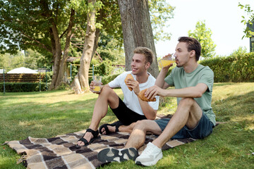 Two joyful friends relax on a blanket, sipping refreshing drinks and sharing moments together.