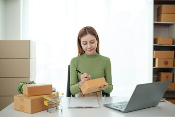 A woman is sitting at a desk with a laptop and a stack of cardboard boxes