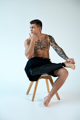 A tattooed young man sits on a stool, showcasing his prosthetic leg and deep in thought in a studio.