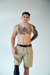 A confident young man with intricate tattoos showcases his prosthetic leg in a minimalist studio...