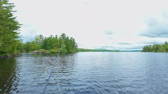 Angler casting rod with artificial baitfish lure for big mouth bass in the early morning, while trolling on inflatable dinghy boat. Fisherman hand holding tackles with lake nature on the background.