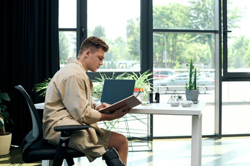 A young man with a prosthetic leg focuses intently on his work in a contemporary office environment.