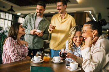 Group of female friends drinking coffee at the restaurant while the guys in the back try to flirt and send them drinks. Girl giggle and gossip about them.