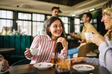 Group of female friends drinking coffee at the restaurant while the guys in the back try to flirt and send them drinks. Girl giggle and gossip about them.