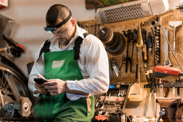 Focused Mechanic in Workshop Checking Mobile Phone While Surrounded by Tools