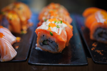 Salmon sushi topped with sauce and mayonnaise is arranged on a tray, ready for customers to serve themselves.