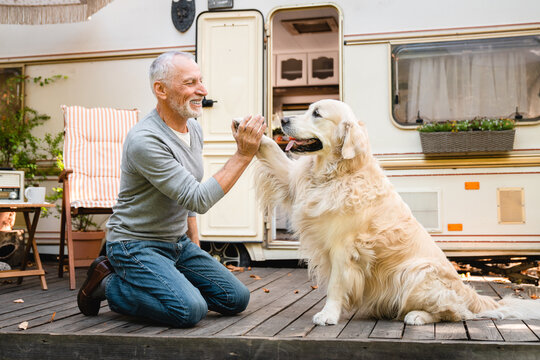 Senior pet owner walking a dog, golden retriever labrador, together on the porch of trailer