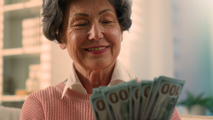 Happy smiling rich Caucasian old woman count money at home bills winning bonus grandmother counting dollars senior granny holding cash old female elderly retired lady with banknotes financial savings