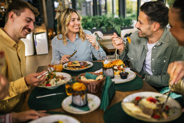 Group of happy friends eating lunch together in a restaurant. They eat delicious salads,...