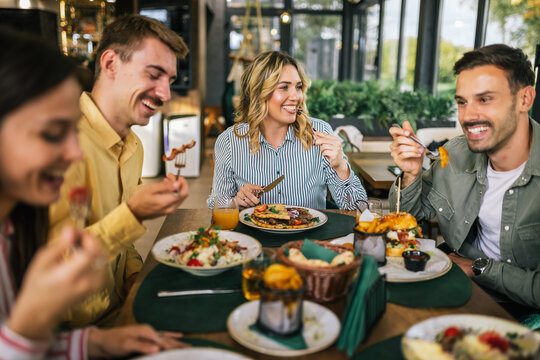 Group of happy friends eating lunch together in a restaurant. They eat delicious salads, hamburgers, bread and meat.
