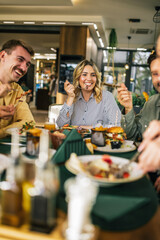Group of happy friends eating lunch together in a restaurant. They eat delicious salads,...