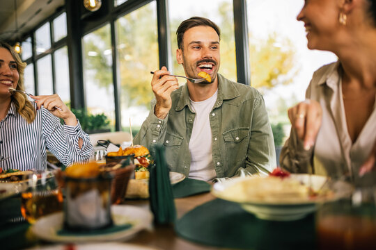 Group of happy friends eating lunch together in a restaurant. They eat delicious salads, hamburgers, bread and meat.