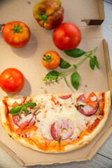 cooked pizza with salami and sausage in a box on a wooden table
