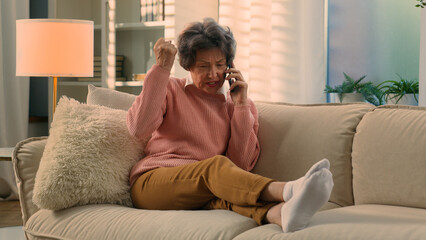 Obraz premium Caucasian mad aggressive dissatisfied old woman senior lady mature retirement granny elderly female at couch at home talk angry mobile phone call talking conflict misunderstanding quarrel smartphone