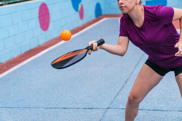 Young woman playing pickleball, hitting the ball with paddle on court