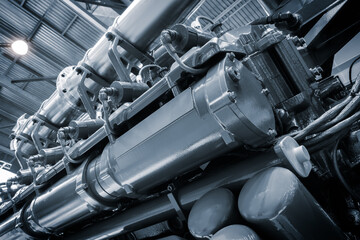 A large engine with many parts is shown in a factory. The engine is made of metal and has a lot of pipes and valves. Concept of industrialization and the complexity of machinery
